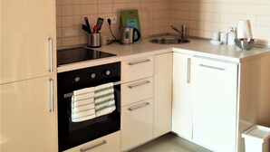 A modern kitchen with white cabinets, a black oven, and a microwave. There is a sink with a faucet, a kettle, and a coffee maker on the countertop.