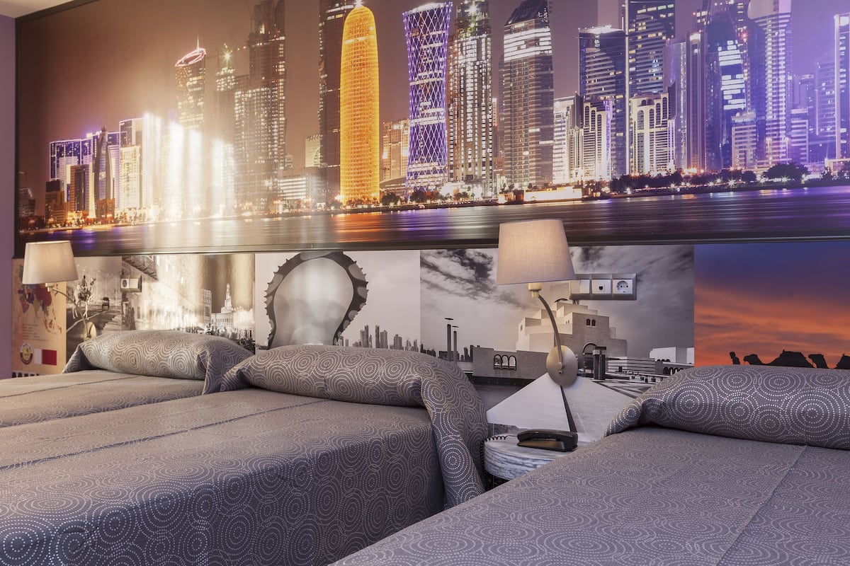 A hotel room with two beds, a cityscape mural on the wall, and a view of the city skyline.