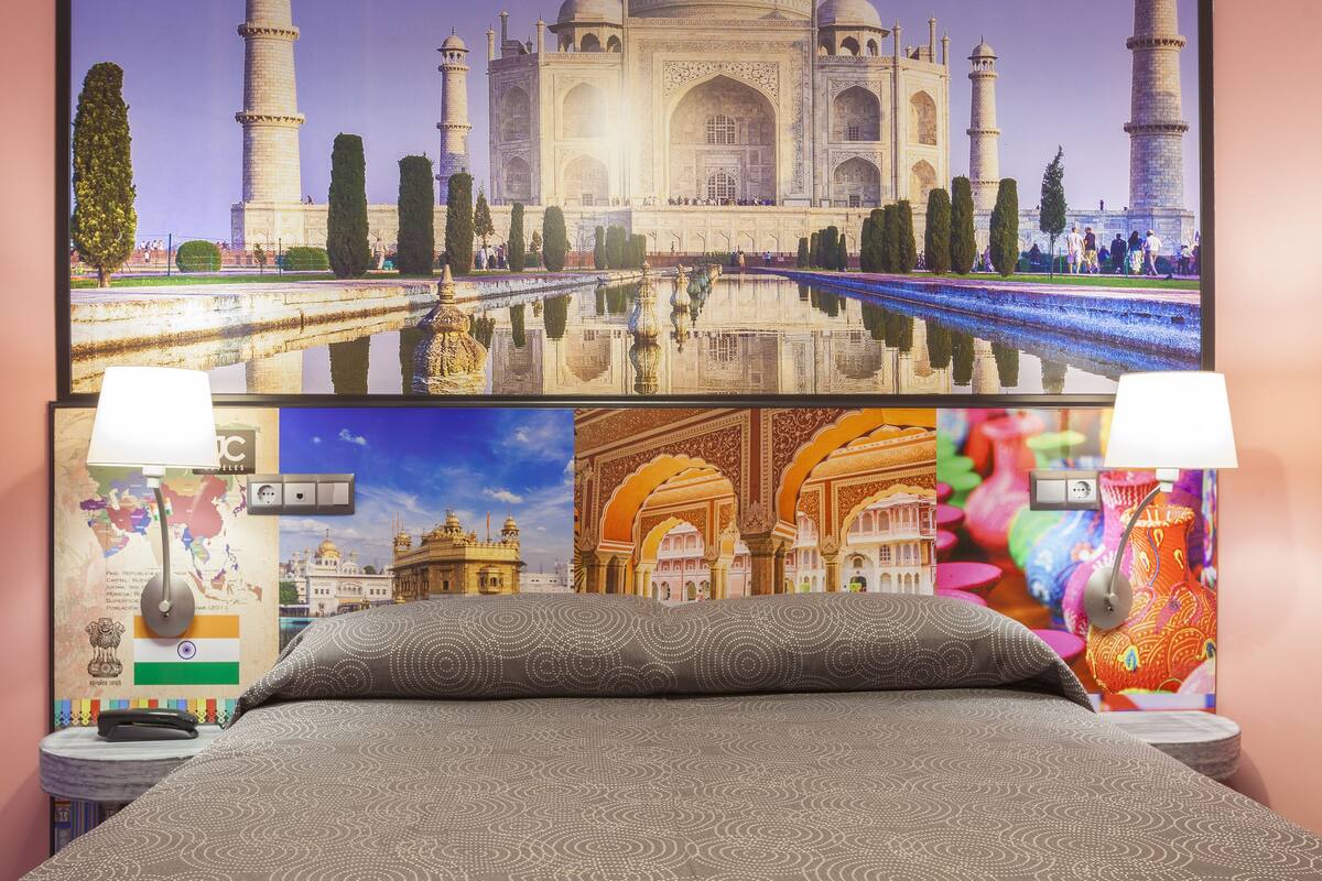 A hotel room with a large bed, a wall with a Taj Mahal mural, a map, and a colorful vase.