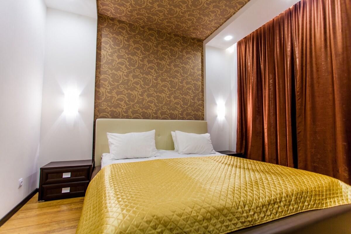 A hotel room with a bed, nightstands, and a patterned wall.