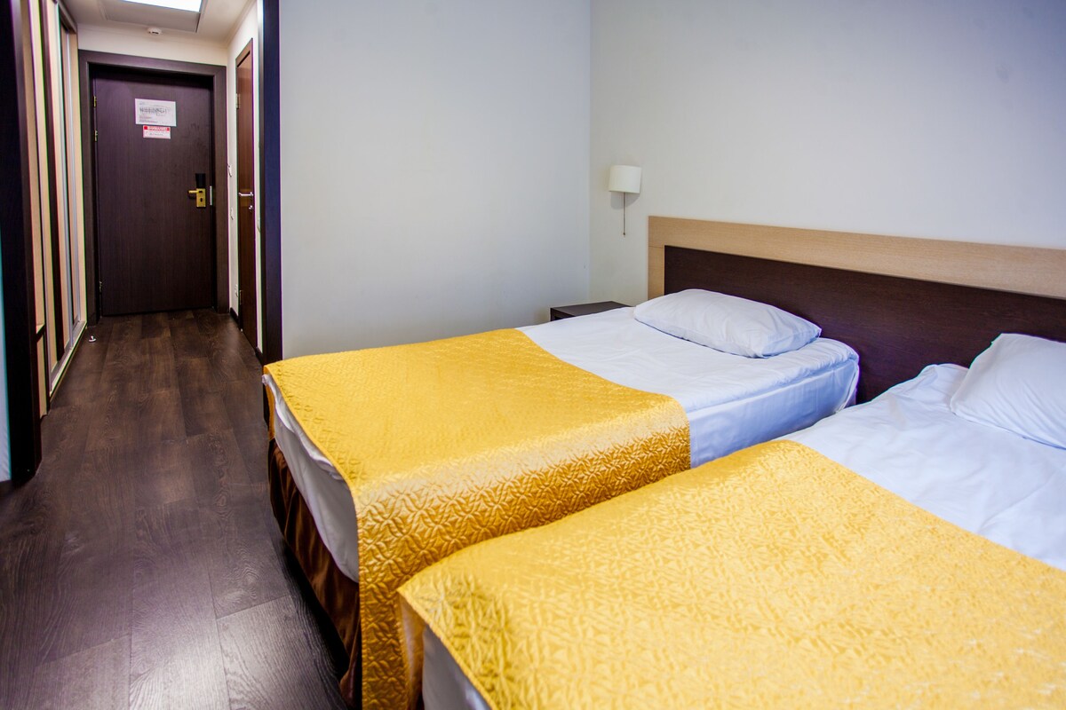 A hotel room with two beds, a wooden headboard, a nightstand, a lamp, and a door with a sign.