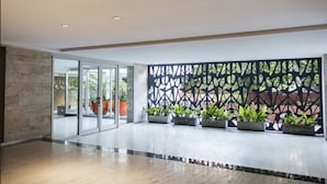 Un hall d’entrée spacieux au design moderne, agrémenté d’une cloison en verre, de plantes en pot et d’un mur à motifs.