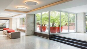 Un hall d’entrée spacieux, doté de grandes fenêtres, d’un escalier et d’un coin salon avec des coussins rouges.