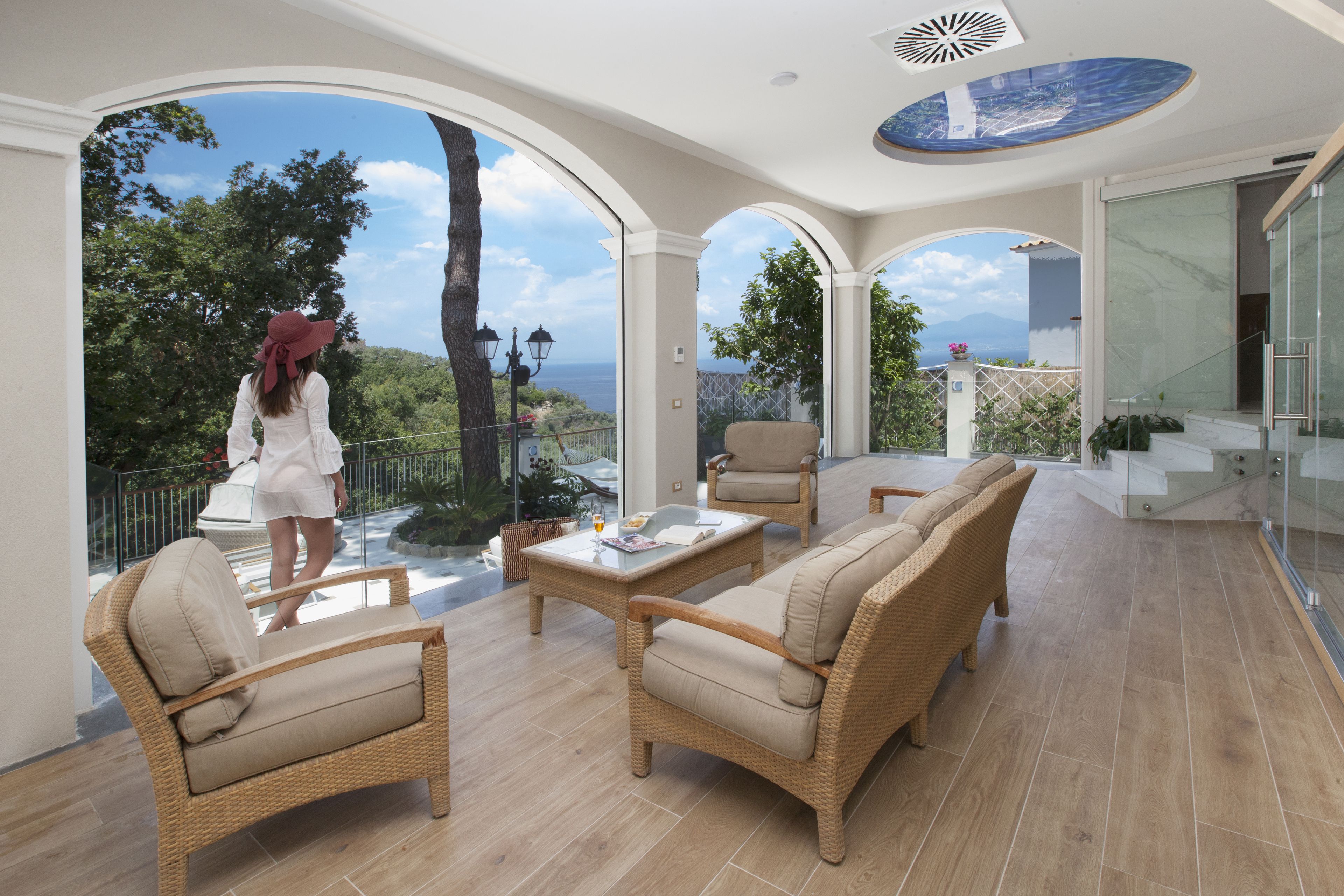 A spacious balcony with wicker furniture, a glass balustrade, and a view of the sea.