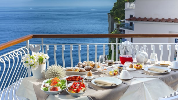Una mesa puesta con diferentes platos y bebidas en un balcón con vistas al mar.