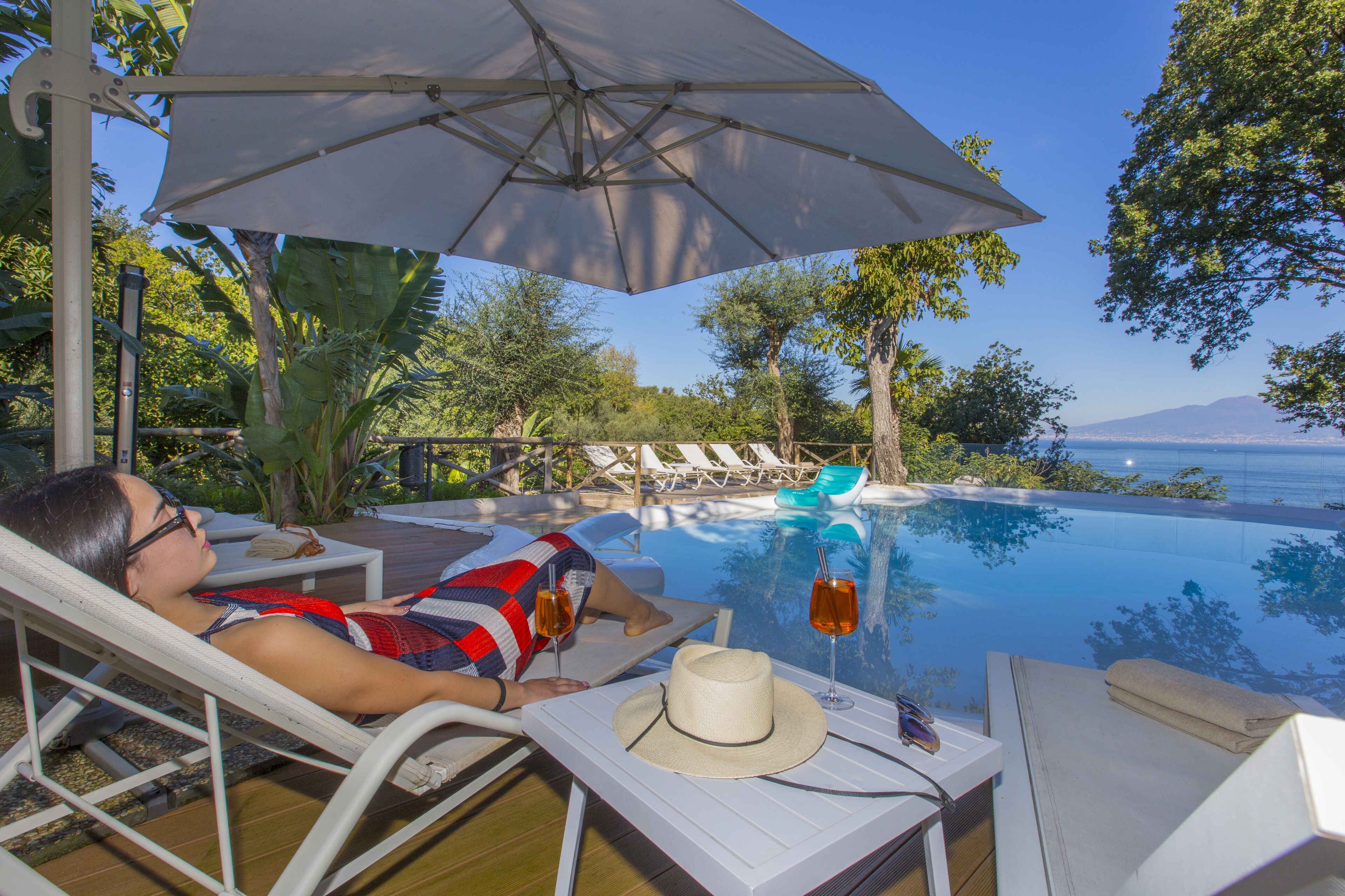 A person relaxing by a poolside with a view of the sea and mountains.