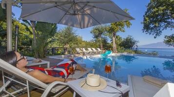 A person relaxing by a poolside with a view of the sea and mountains.