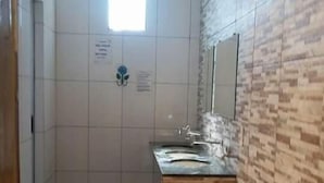 Une petite salle de bain avec une douche, un lavabo et un miroir. Il y a une fenêtre au-dessus du lavabo et une porte sur le côté gauche.