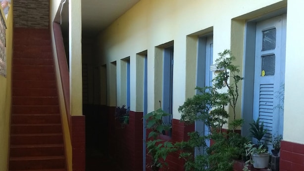 Un couloir au sol carrelé, un escalier sur la gauche et des plantes en pot le long des murs.