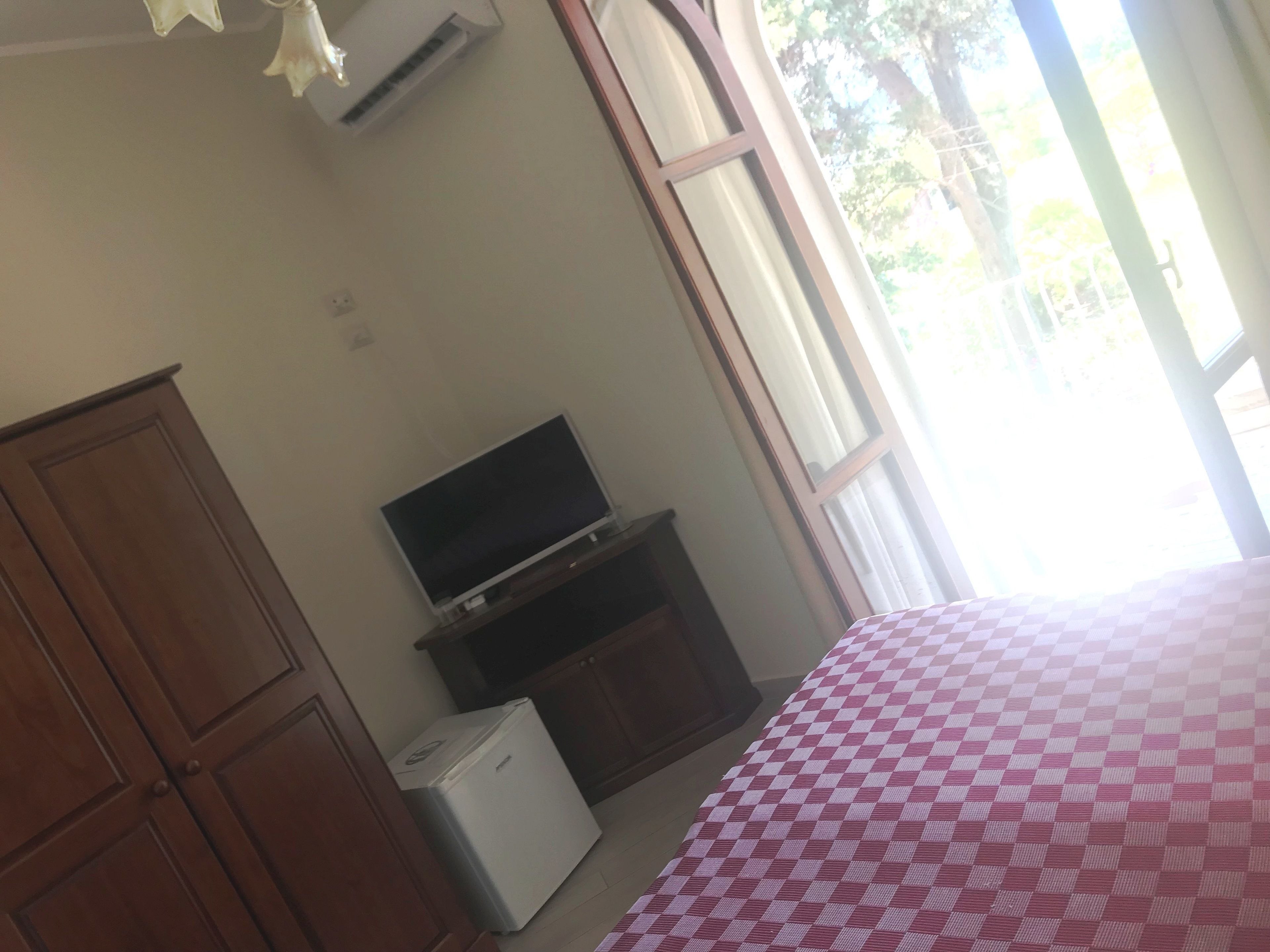 A room with a bed, a television on a stand, a small refrigerator, and a wooden wardrobe.