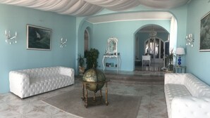 Een ruime kamer met een grote witte bank, een wereldbol op een standaard en een spiegel op een voetstuk.