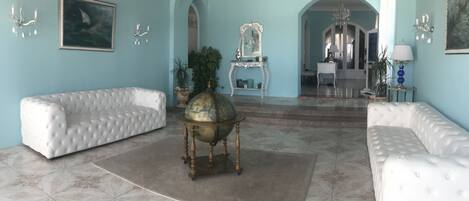 A spacious room with a large white sofa, a globe on a stand, and a mirror on a pedestal.