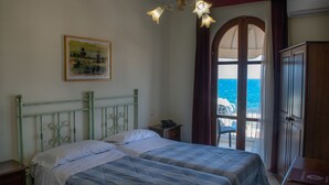 Een slaapkamer met een bed, een nachtkastje, een garderobe en uitzicht op zee door een raam.