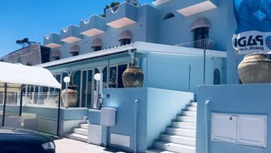 Een hotelentree met een modern ontwerp, met een trap naar de hoofdingang, grote plantenbakken en een heldere blauwe lucht.