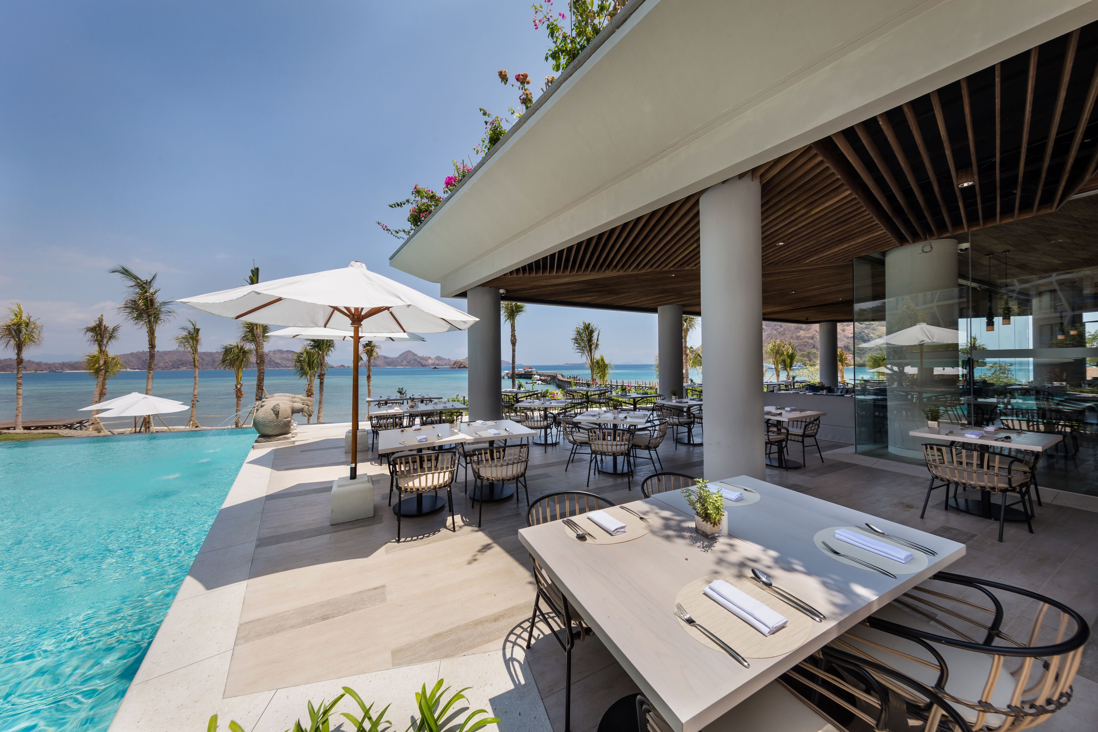 Un área de comedor junto a la piscina con mesas y sillas, con vistas a la piscina y a la vista panorámica del océano.