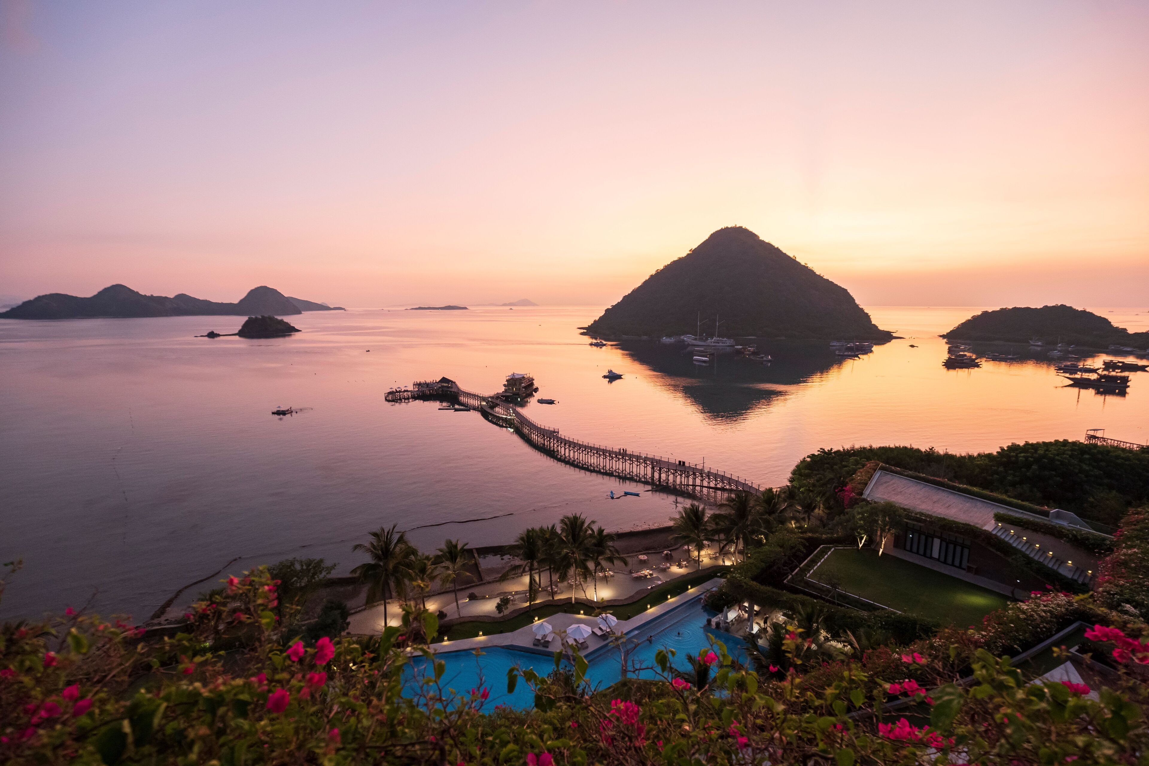 A resort with a swimming pool, a dock, and a view of the sea at sunset.