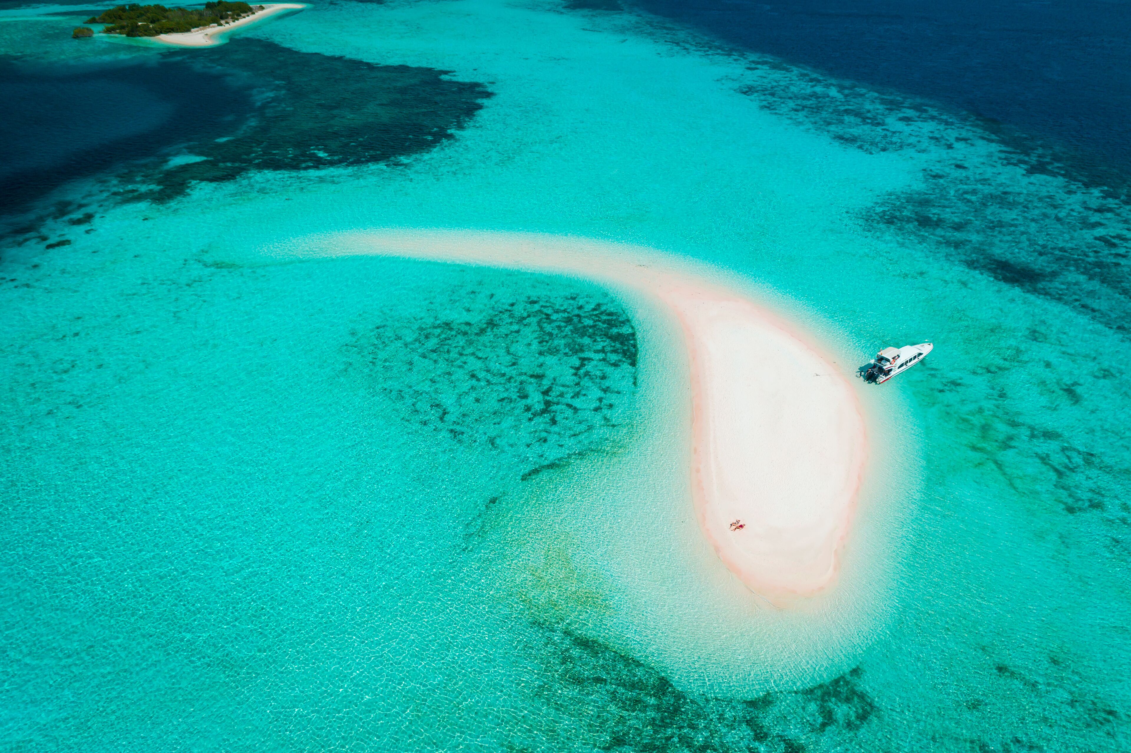 An aerial view of a turquoise lagoon with a boat anchored near a sandy beach.