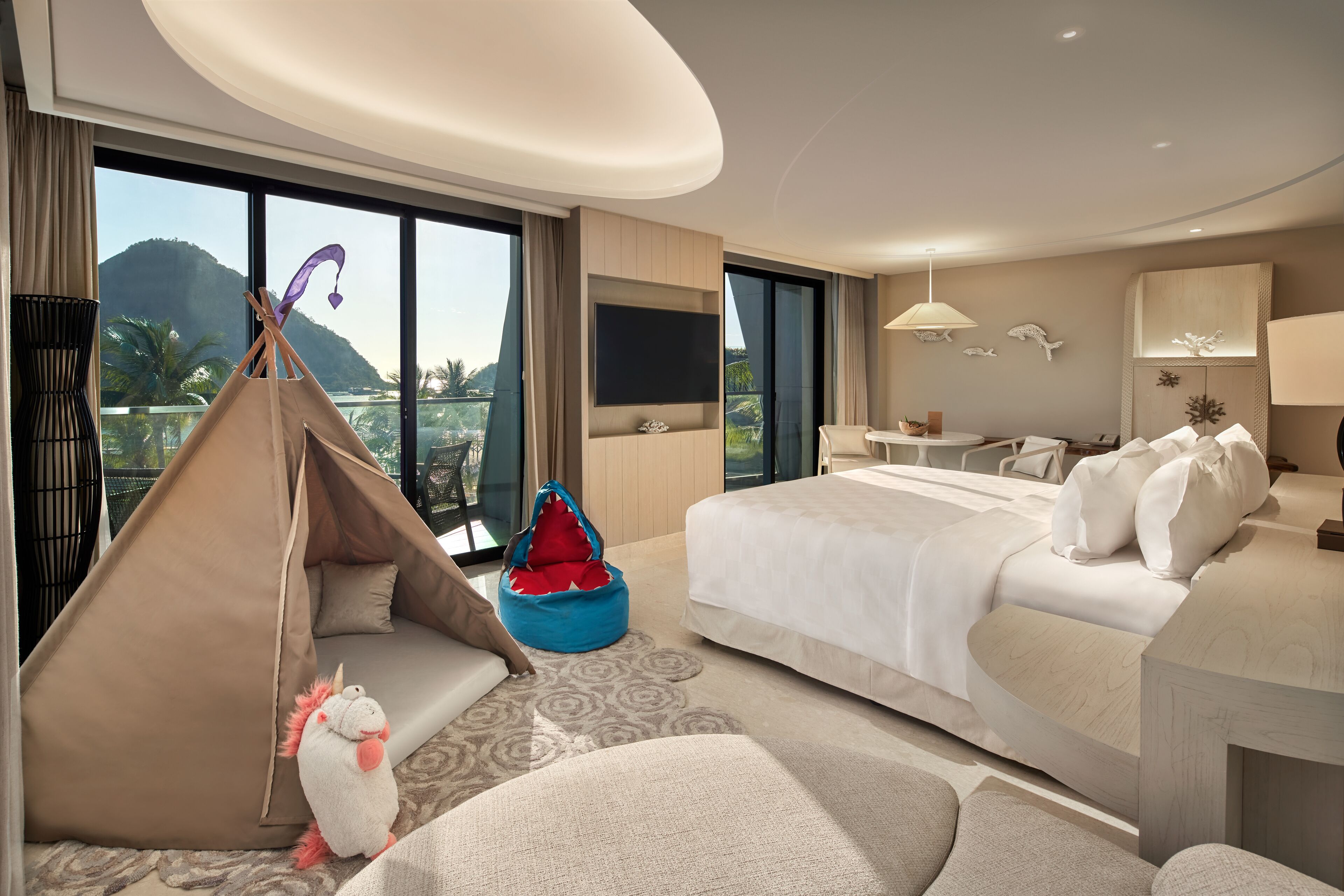 A modern hotel room with a large bed, a sofa, a tent, and a view of a mountain.
