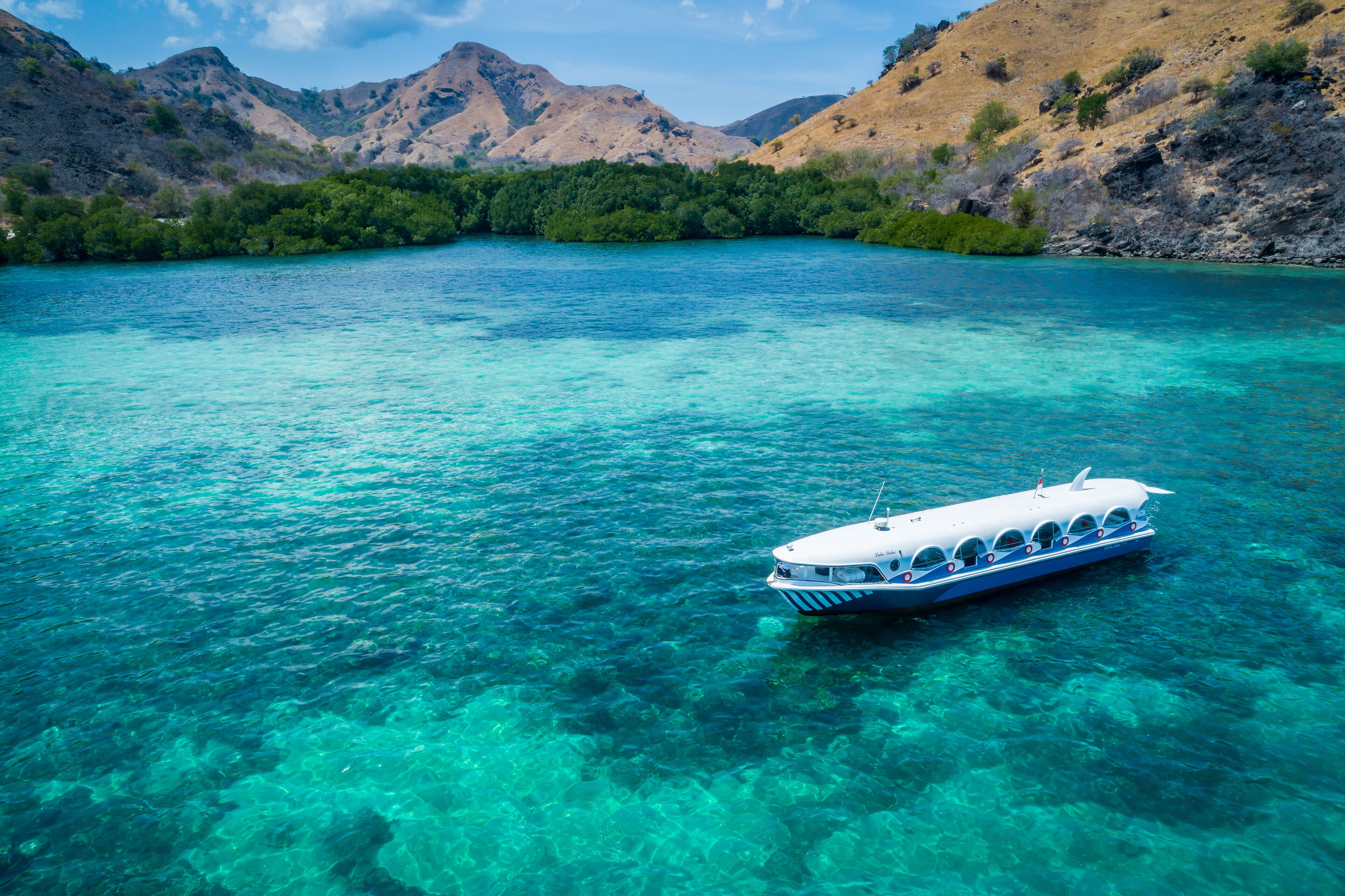 A boat on clear turquoise water surrounded by hills.