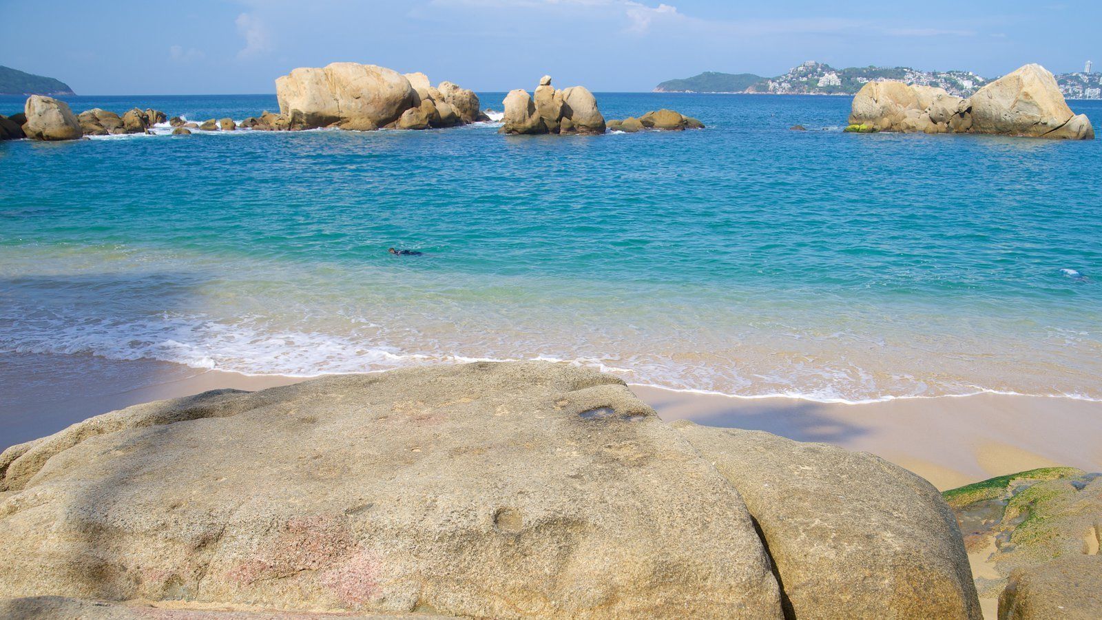Una playa con grandes rocas y agua azul cristalina.