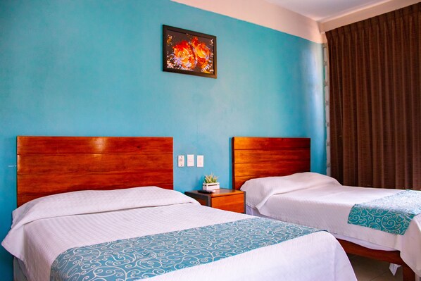 Habitación de hotel con dos camas, cabecero de madera, pared azul, un cuadro y una ventana con cortinas.
