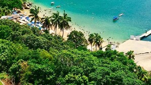 Una zona costera con playa, embarcaciones y abundante vegetación.