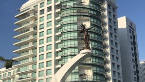 Un hotel moderno de gran altura con fachada curva, varios balcones y una estatua destacada en la entrada.