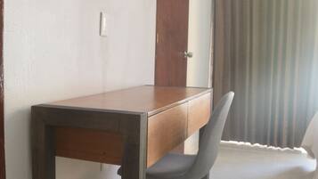 A room with a wooden desk, a grey chair, a flat-screen TV mounted on the wall, and an air conditioning unit.
