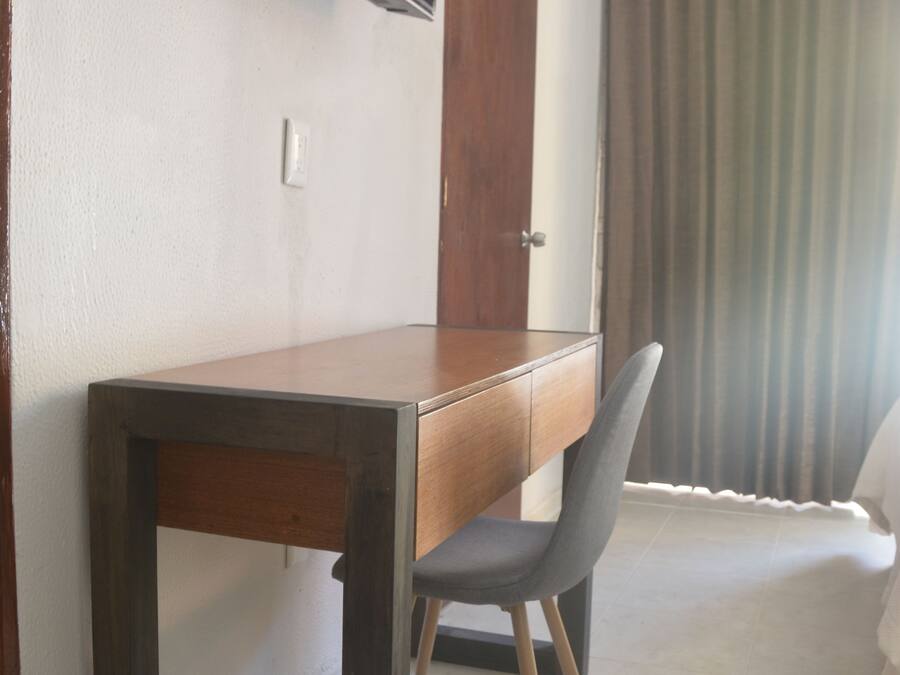 A room with a wooden desk, a grey chair, a flat-screen TV mounted on the wall, and an air conditioning unit.