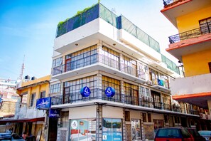 Un hotel de varios pisos con balcones, una señalización visible del hotel y vista a la calle.