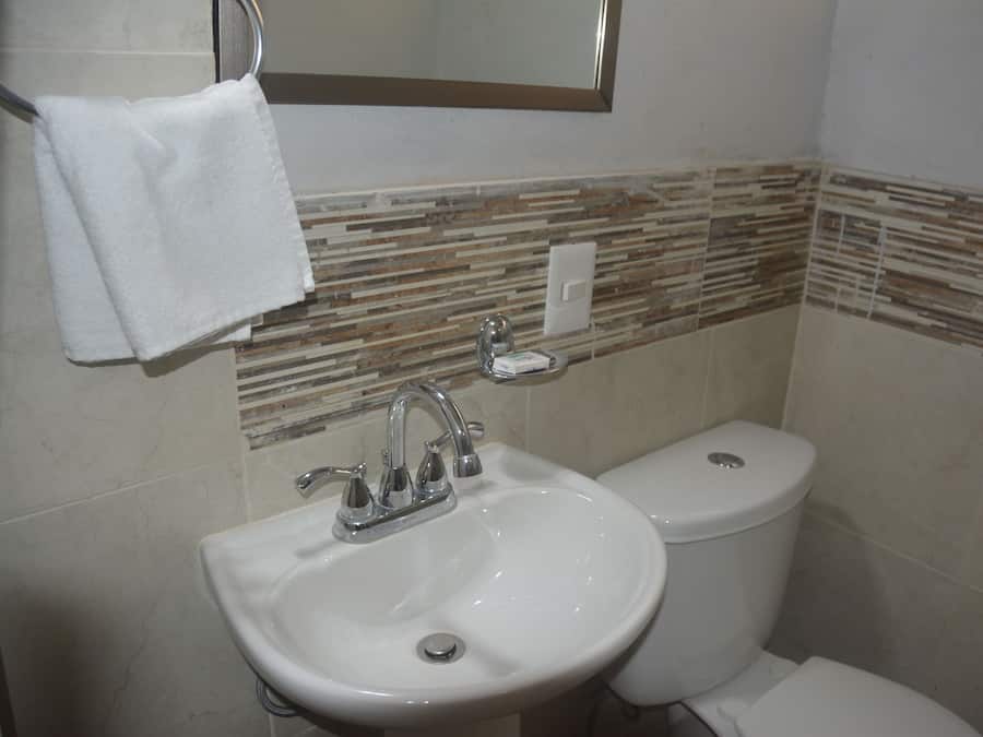 Un baño con un lavamanos blanco, un inodoro y una toalla colgada en un perchero.