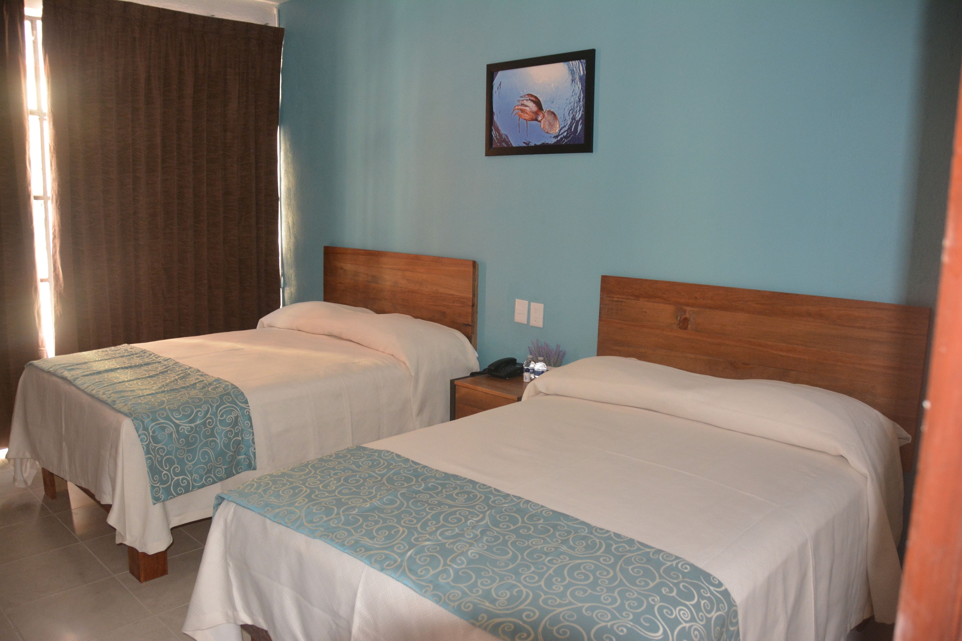 Two single beds with wooden headboards, a nightstand with a phone and a small vase, and a painting on the wall.