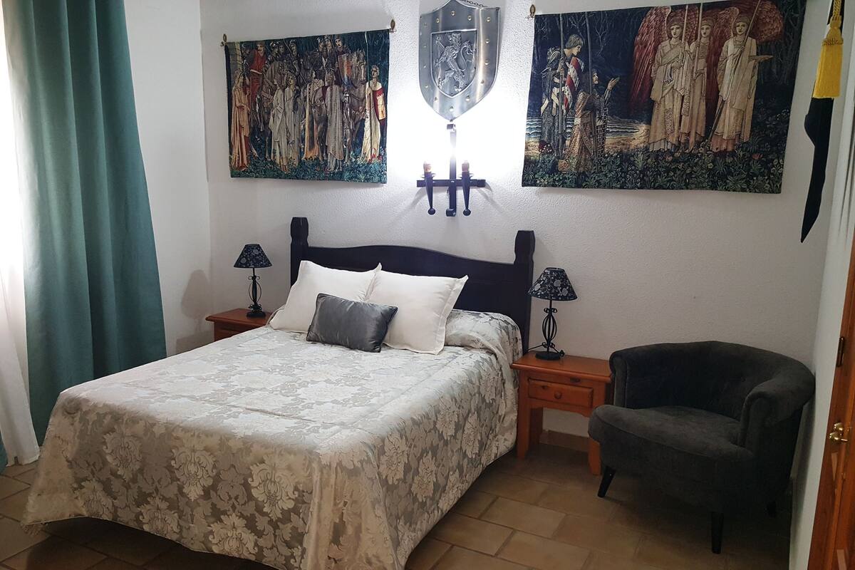 A bedroom with a bed, two nightstands, a chair, and two paintings on the wall.