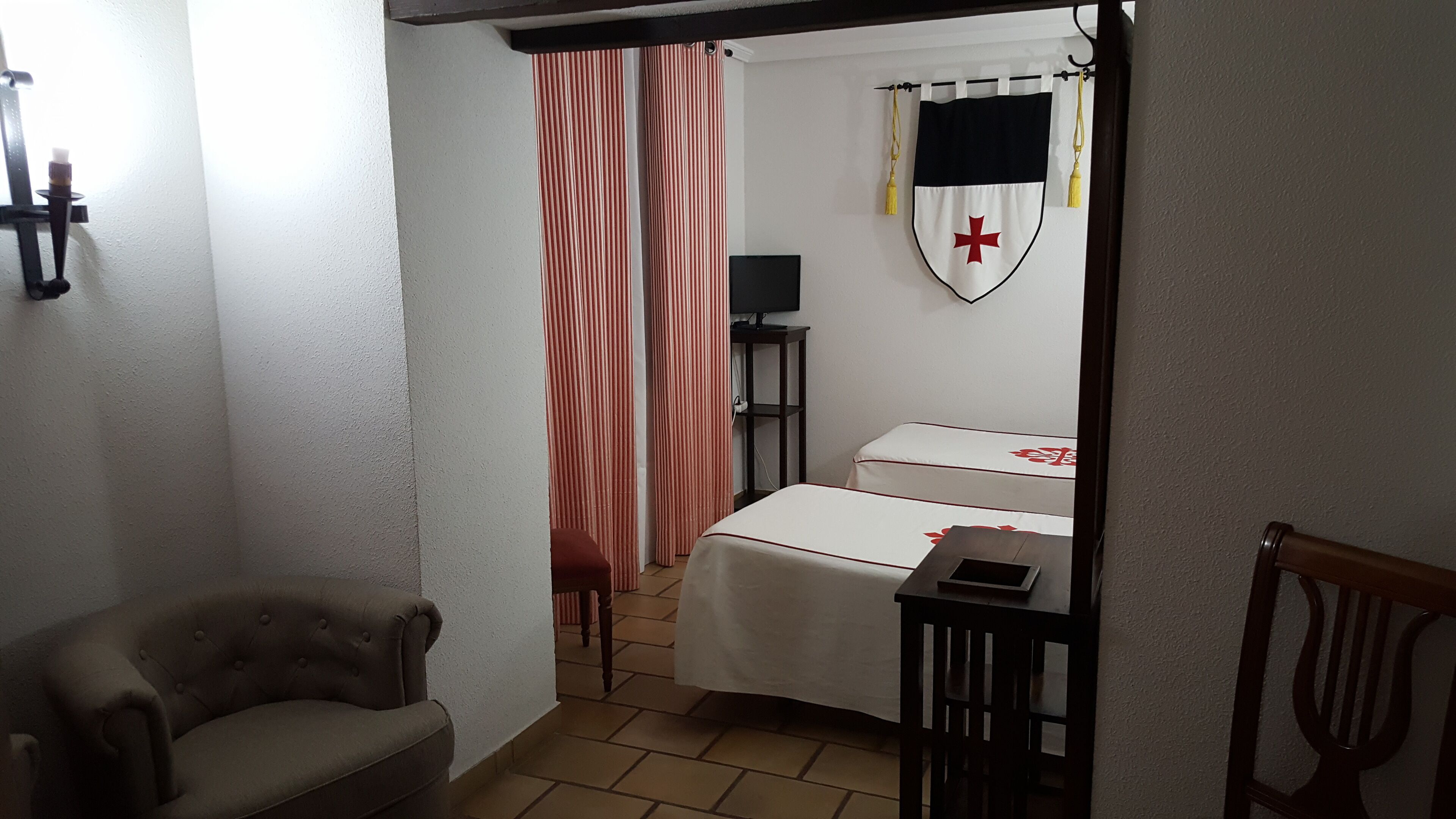Une pièce comprenant un lit, une chaise, une petite table, un téléviseur et un rideau.