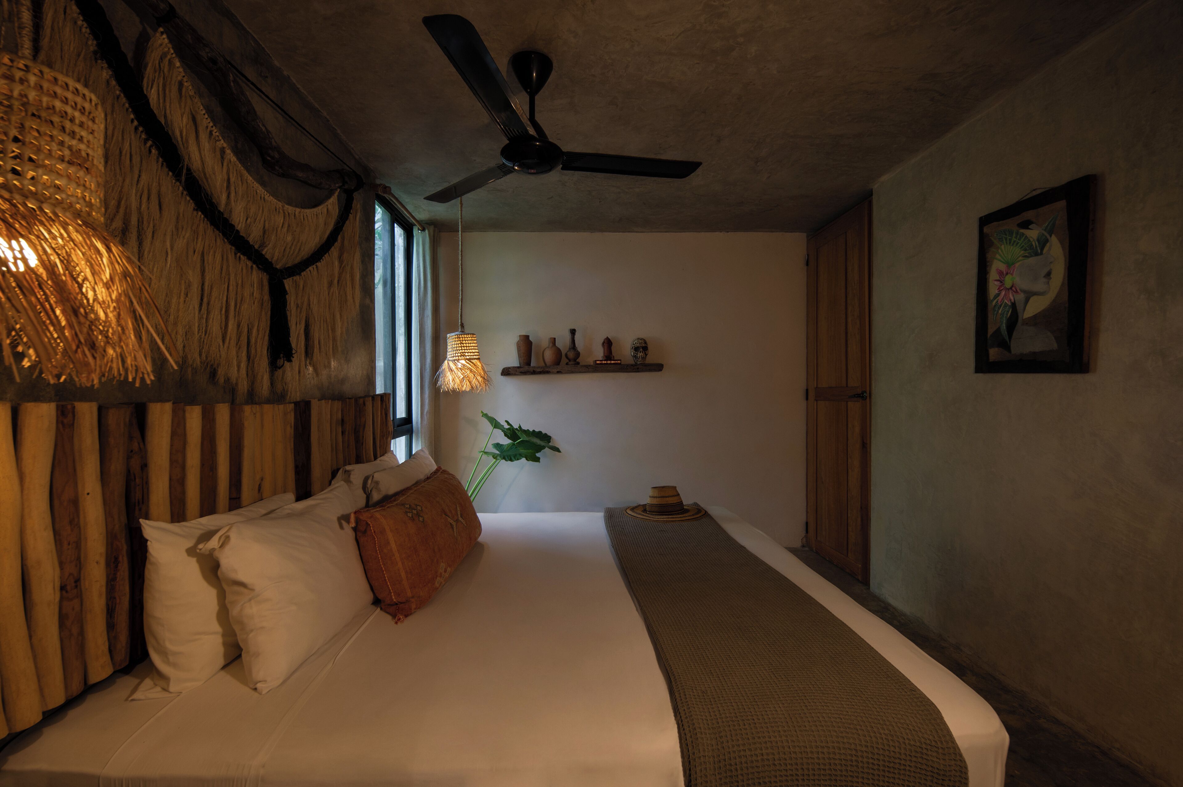 A bedroom with a bed, a ceiling fan, a wall-mounted shelf with decorative items, and a window with natural light.