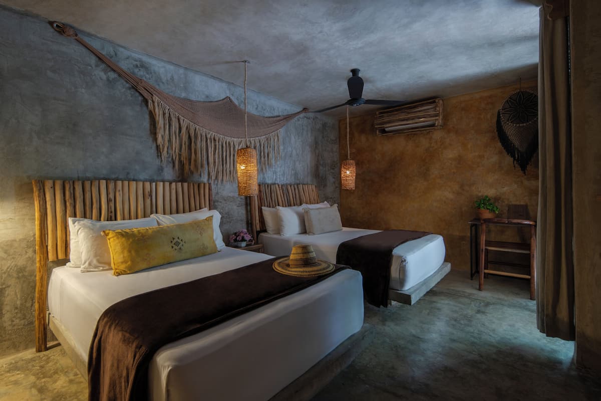 Ein Zimmer mit zwei Betten, einer Hängematte, hängenden Lampen, einem Deckenventilator und einem kleinen Tisch mit einer Pflanze.