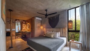 Un dormitorio con una cama grande, un ventilador de techo, una ventana con cortinas, una mesita de noche y una alfombra.