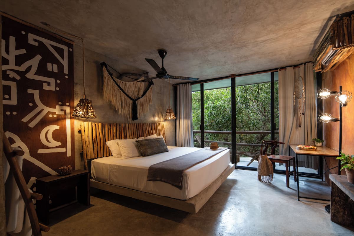 Ein modernes Schlafzimmer mit einem großen Bett, einem Deckenventilator und Blick auf Grünflächen.