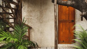Una puerta de madera rústica con un picaporte metálico, un muro de hormigón y una escalera de madera.