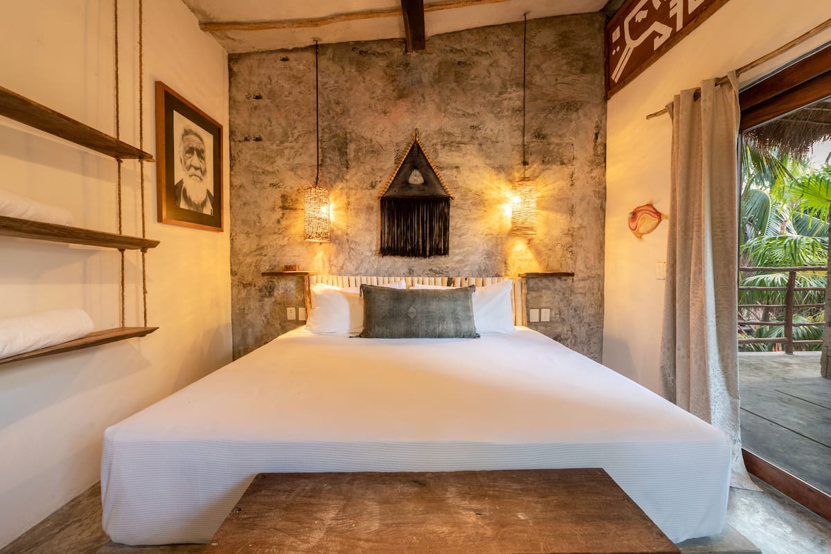 Ein großes Bett mit Holz-Kopfteil, zwei Wandleuchten und ein gerahmtes Bild an der Wand.