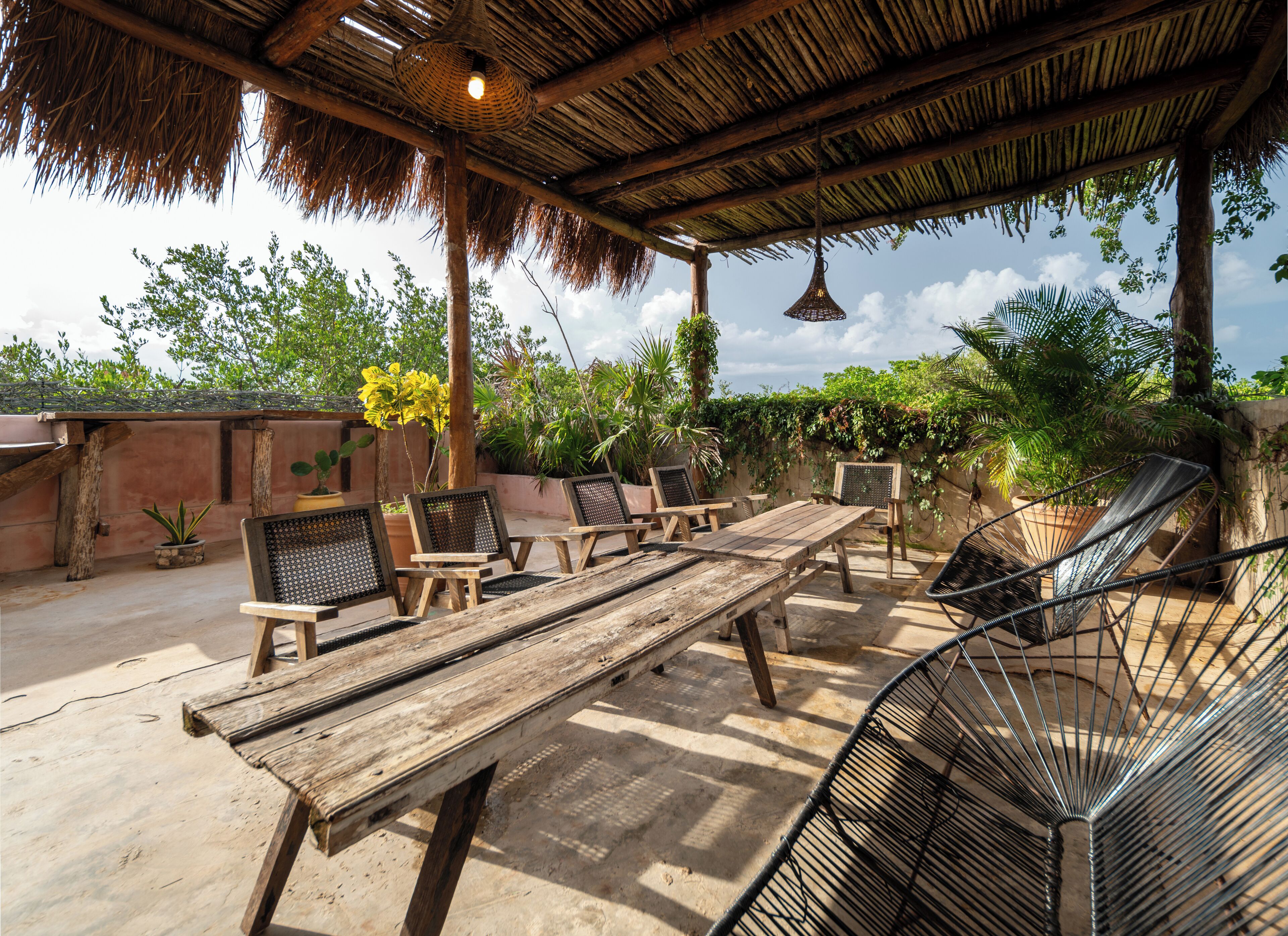 An outdoor patio with wooden furniture, a thatched roof, and potted plants.