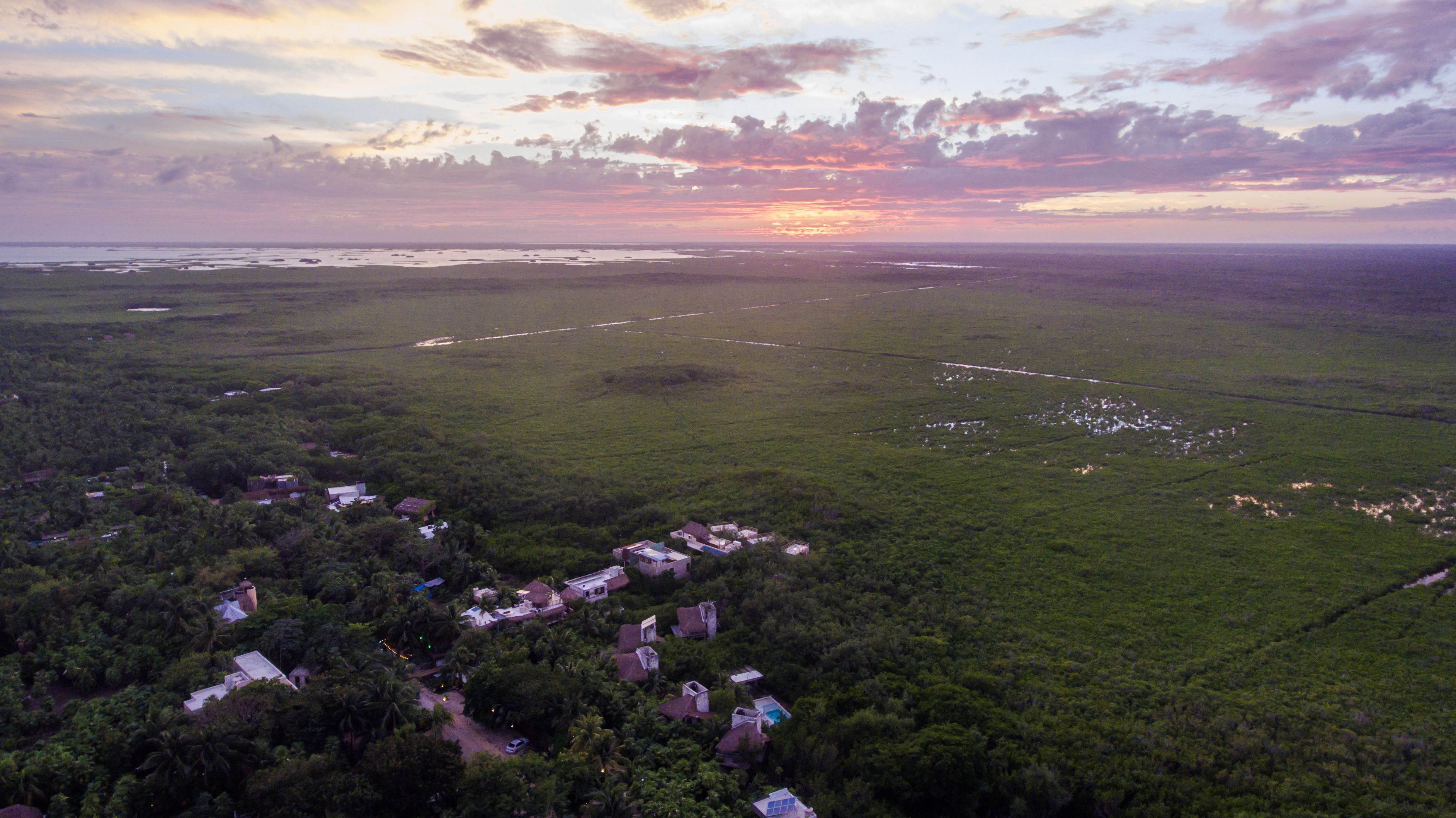 Une vue aérienne d’une zone rurale où l’on aperçoit des maisons dispersées, entourées d’une végétation luxuriante.