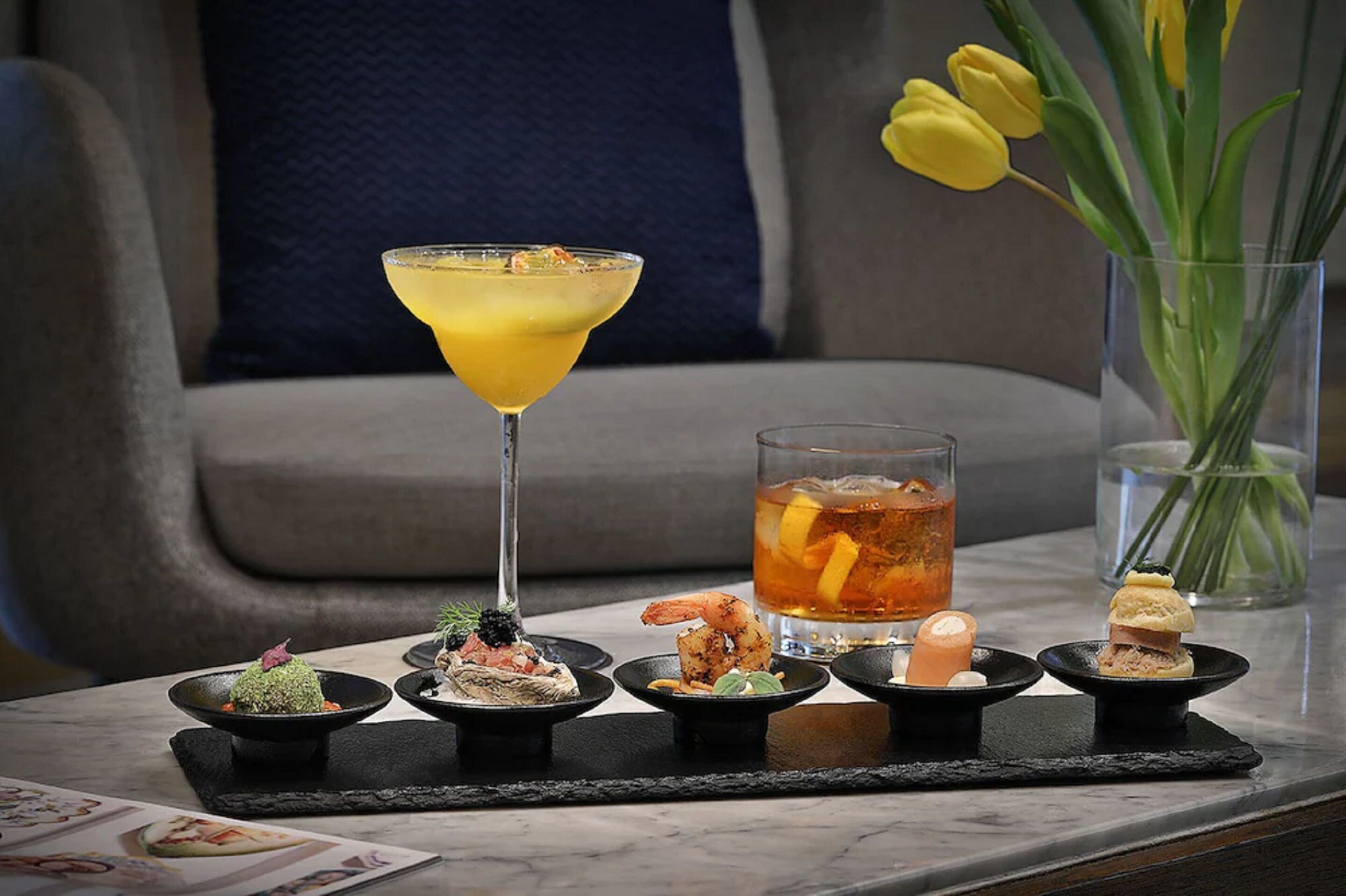 A table with a martini glass, a glass of iced tea, and various small dishes of appetizers.