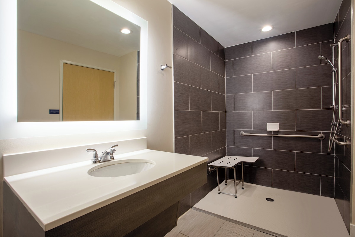 A modern bathroom with a large mirror, a sink, and a shower area.