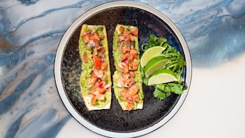 Two avocado toast sandwiches on a plate with a lime wedge and a side salad.