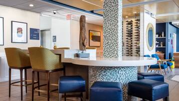 Una zona de bar con taburetes, un pilar central y una estantería de vinos en la pared.