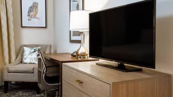 Une chambre d’hôtel avec un bureau en bois, un téléviseur à écran plat, une lampe, une chaise et un tableau encadré au mur.