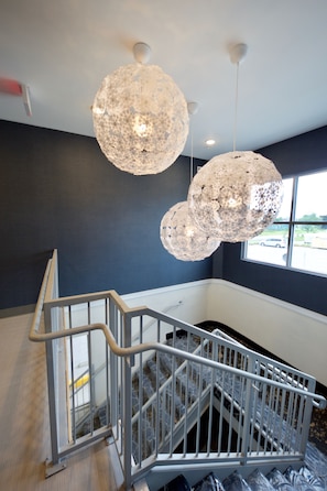 A staircase with a metal railing, a large window with a view of the outside, and two large, textured spherical light fixtures. - voco St. Augustine Historic Area by IHG (St. Augustine)