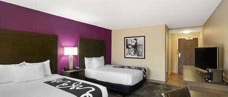 A hotel room with two beds, a desk, a TV, and a framed picture on the wall.