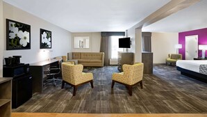 A hotel room with a sofa, two armchairs, a desk with a computer, a flat-screen TV, and a bed. - La Quinta Inn & Suites by Wyndham Columbus MS (Columbus)